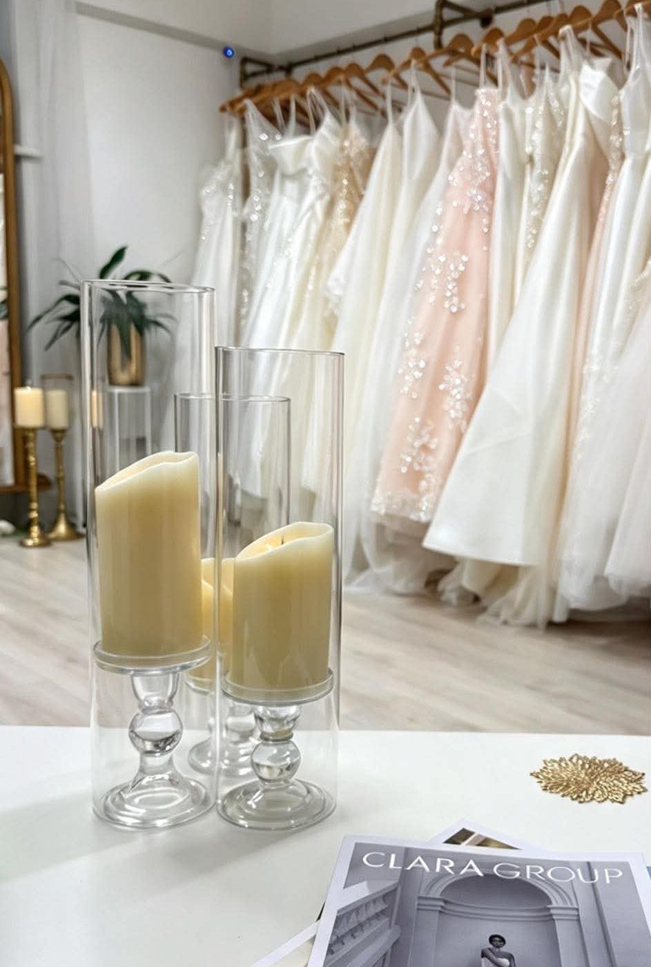 Rails of ivory and blush wedding gowns behind candles and designer brochures